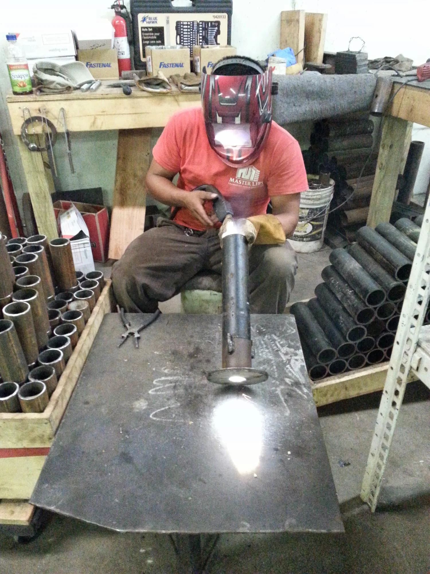 Technician in red shirt installing steel foundation pier with welding helmet in workshop