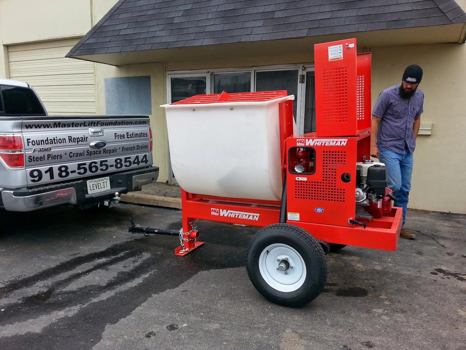Red Whiteman concrete mixer trailer with white drum at residential foundation repair job site