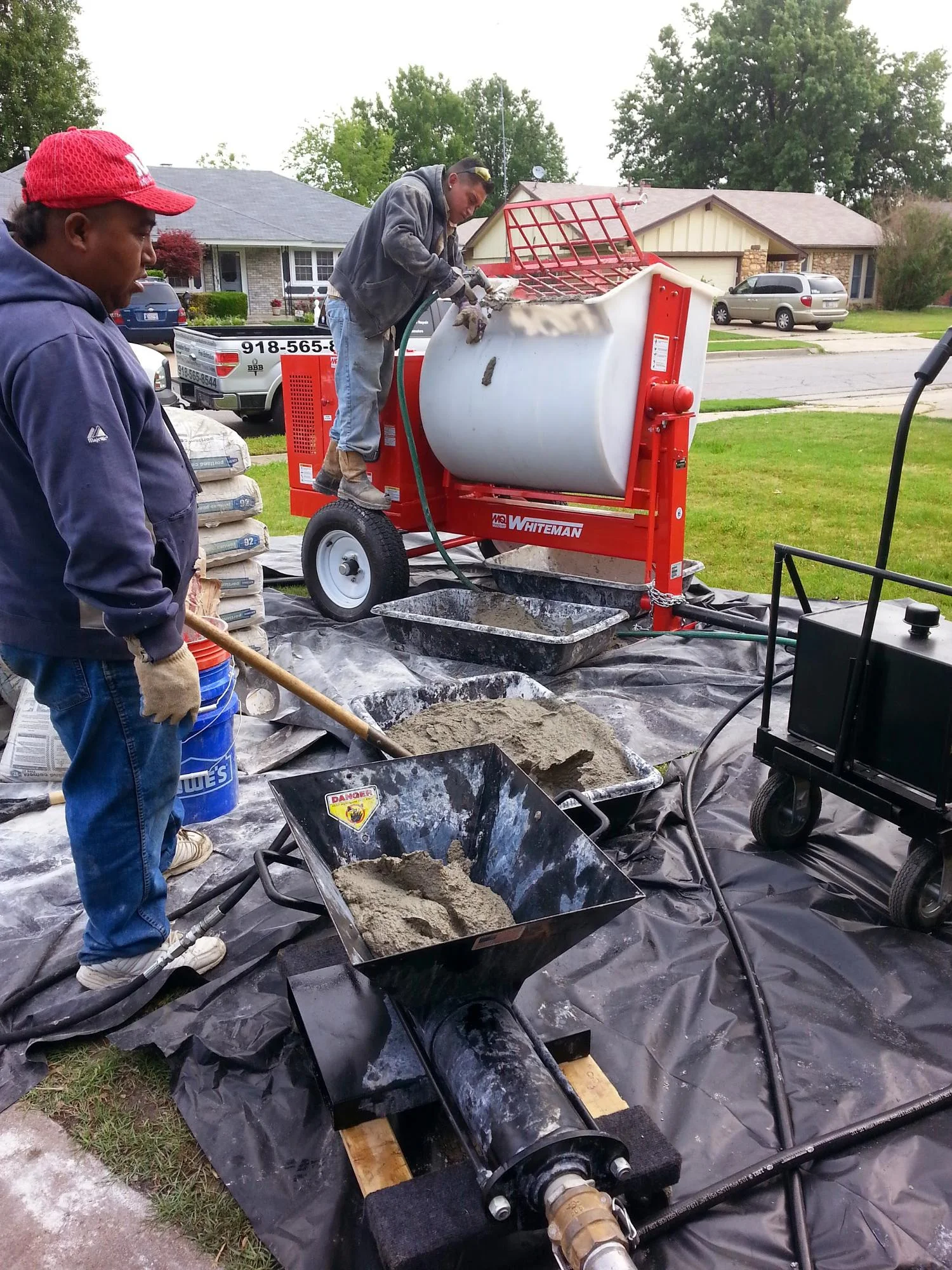Concrete mixer and crew preparing materials for foundation repair work in residential driveway