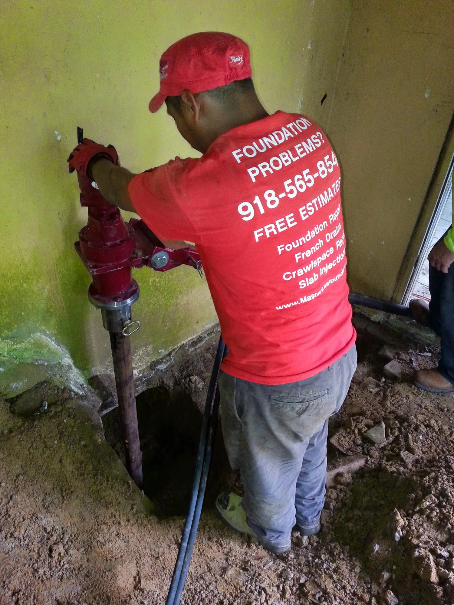 Foundation repair technician inspecting red support post in basement with yellow walls