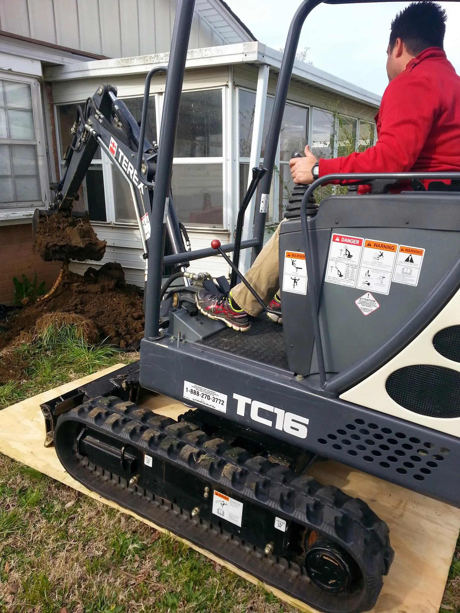 Bobcat TC16 track loader excavating soil near residential foundation for inspection and repair work