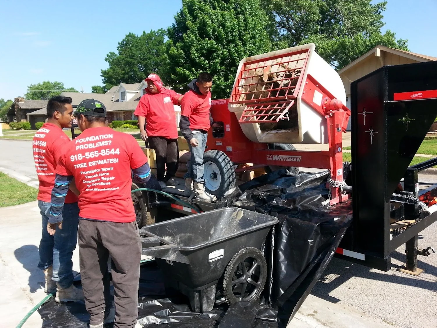 Foundation repair crew with red Whiteman equipment trailer at residential property