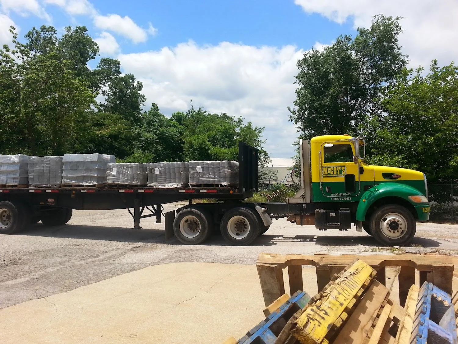 Yellow and green delivery truck with flatbed trailer loaded with palletized foundation materials